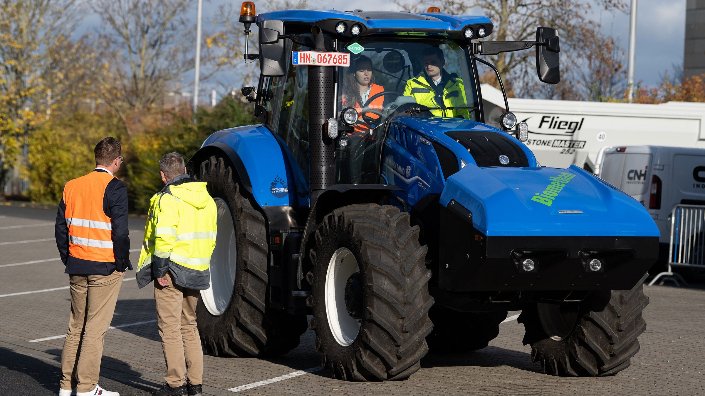 Zwei Männer vor einem Biomethan Traktor stehend beobachten zwei Personen, die in einem Biomethan Traktor sitzen